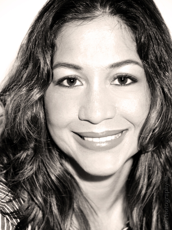 A high exposure greyscale headshot of Duque smiling. It is a close-up headshot. You can only see her from the top of her forehead to the base of her neck.