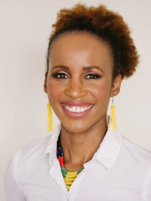 A chest-up photo of Lebo smiling widely at the camera. She is wearing a white button up blouse, colourful multi-layered bead necklace, and yellow tassle earrings. Her hair is pulled back into a single afro puff.
