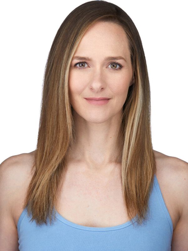 Kristi is seen in a headshot against a stark white background. Her long hair is straight and down - it is brown with blonde highlights in it. She is wearing a baby blue camisole, and looking directly at the camera.